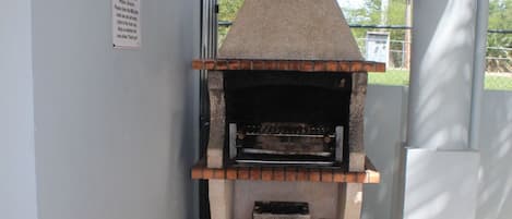 Een kleine, in baksteen opgemetselde oven met schoorsteen, in een smalle ruimte met betegelde vloer en witte muren.