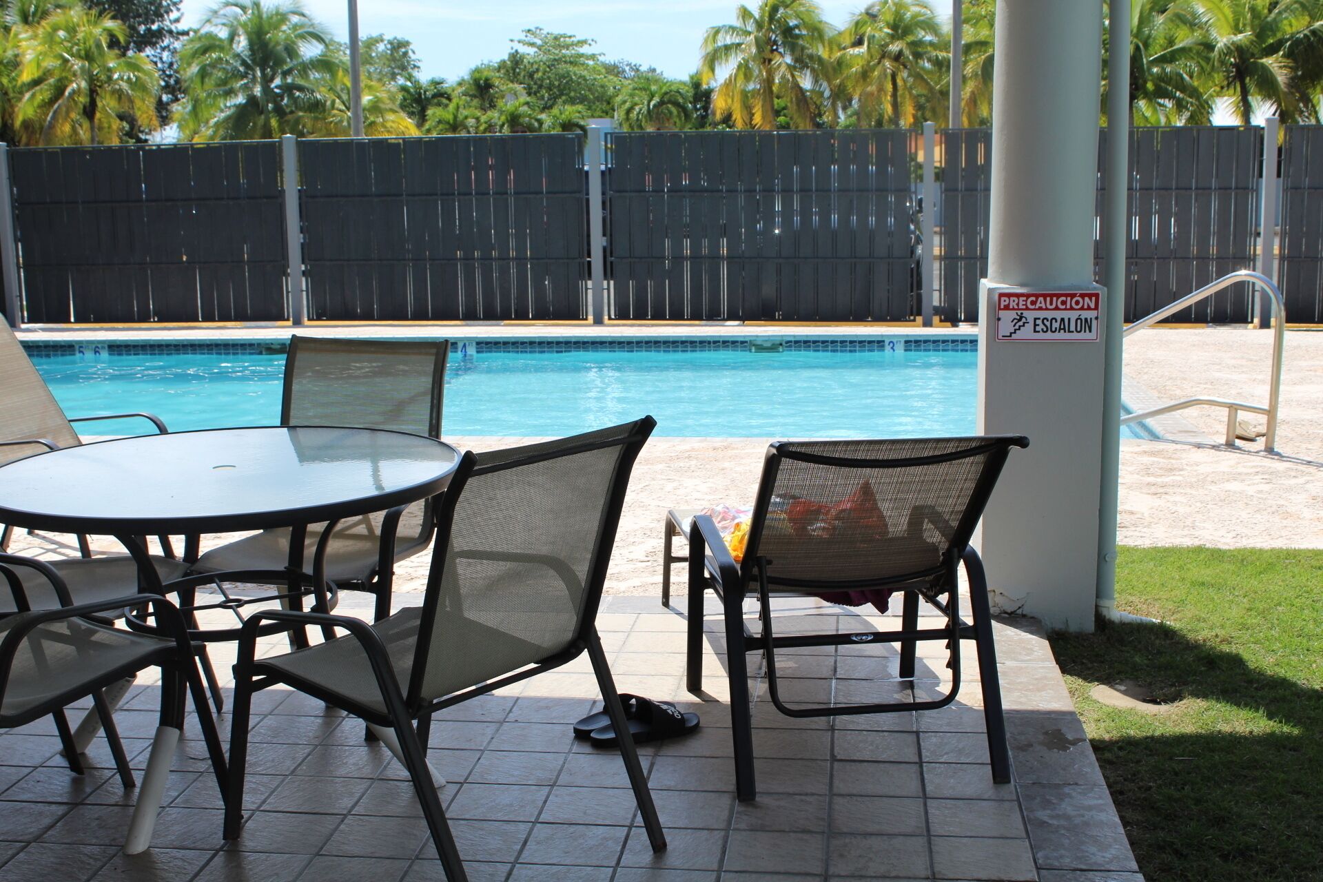 A poolside area with a table and chairs, a pool, and a safety sign.