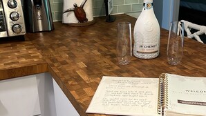 Eine Küchenarbeitsplatte mit Holzoberfläche, eine Flasche JP Chenet Ice, ein Notizbuch und ein Glas.