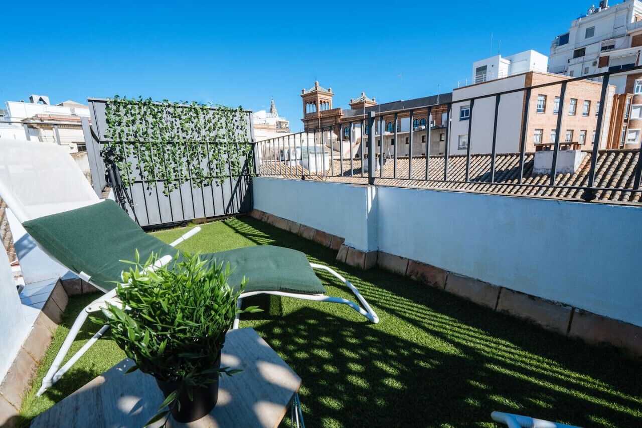 A rooftop terrace with two lounge chairs, a small table, and a potted plant.