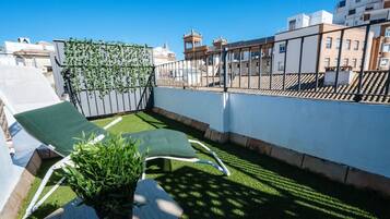 A rooftop terrace with two lounge chairs, a small table, and a potted plant.