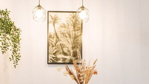 A dining area with a wooden table, four grey chairs, a vase with dried plants, and two hanging pendant lights.