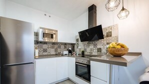 A modern kitchen with a stainless steel refrigerator, a microwave, an oven, and a flat-screen TV mounted above the counter.