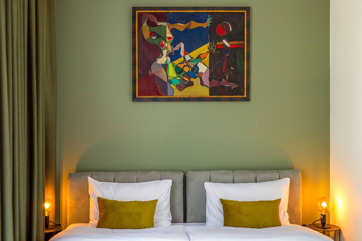 A hotel room with a bed, two bedside lamps, and a painting on the wall.