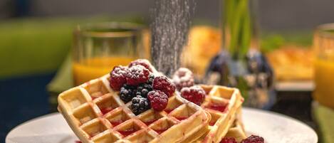 A plate of waffles with berries and powdered sugar, with a hand sprinkling sugar.