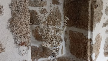 Een stenen muur met een kleine nis waarin een witte metalen vaas met takken staat.