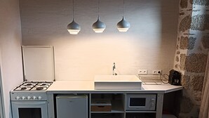 Eine kompakte Küchenzeile mit Herd, Backofen, Mikrowelle, Spüle und drei Pendelleuchten.