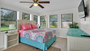 Ein Schlafzimmer mit Bett, Deckenventilator, Fernseher und großen Fenstern.