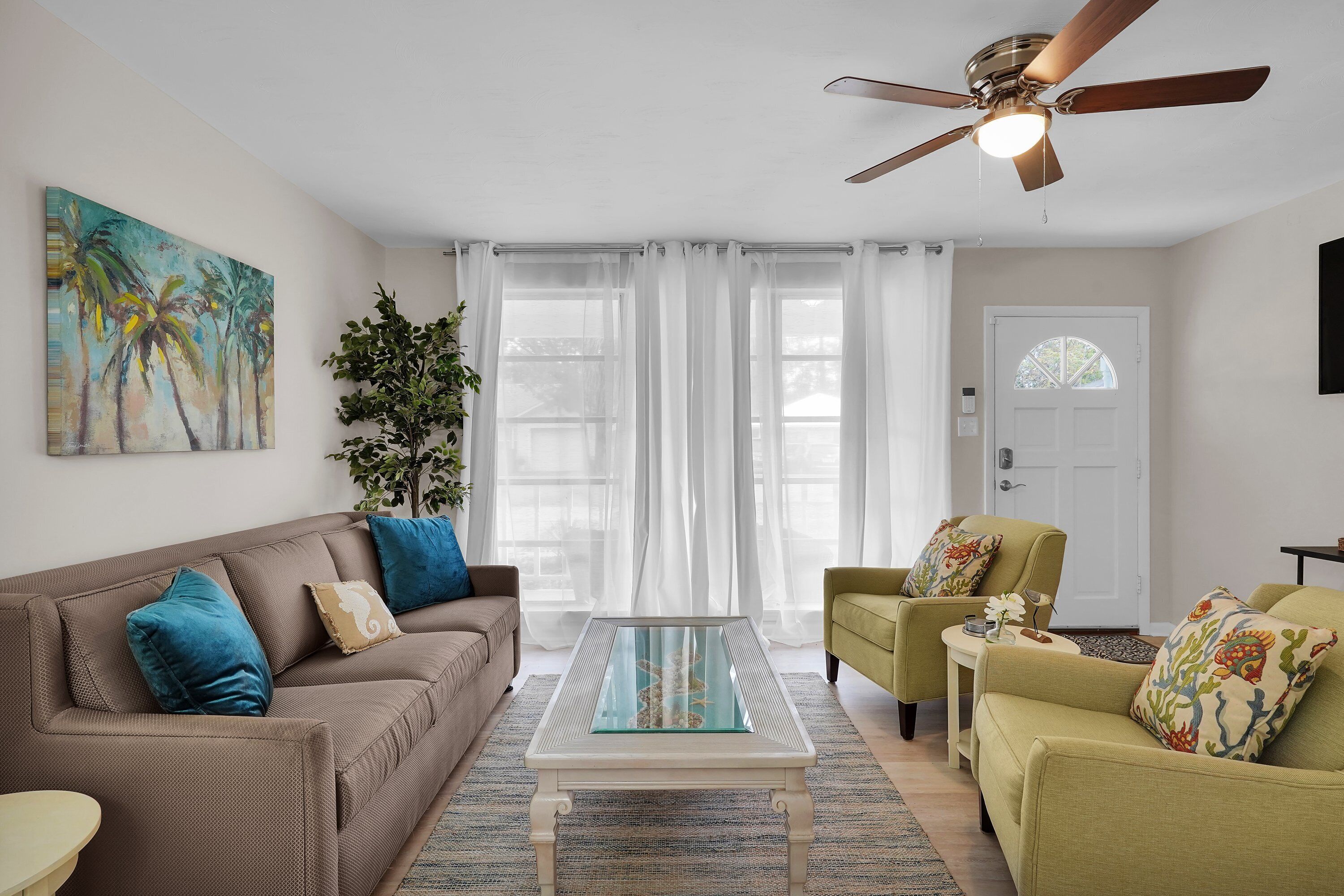 Un salon avec un canapé marron, un fauteuil vert, une table basse en verre et un ventilateur de plafond.