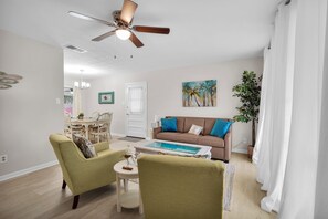 A living room with a ceiling fan, a coffee table, a sofa, and a dining area with chairs and a table. - Cottage w/Heated Pool~10 Mins from Downtown &Beach (St. Augustine)