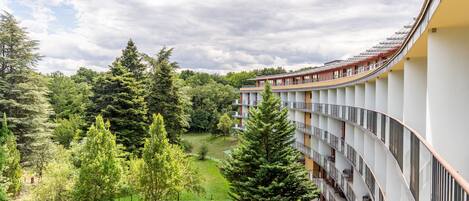 A modern hotel with a curved balcony overlooking a lush green landscape and dense forest.