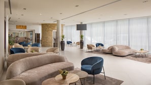 Un hall d’hôtel moderne avec un canapé beige aux lignes courbes, des chaises bleues et un bar en arrière-plan.