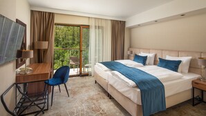 Une chambre d’hôtel équipée d’un lit, d’un bureau, d’une chaise, d’une télévision et d’un balcon donnant sur la verdure.