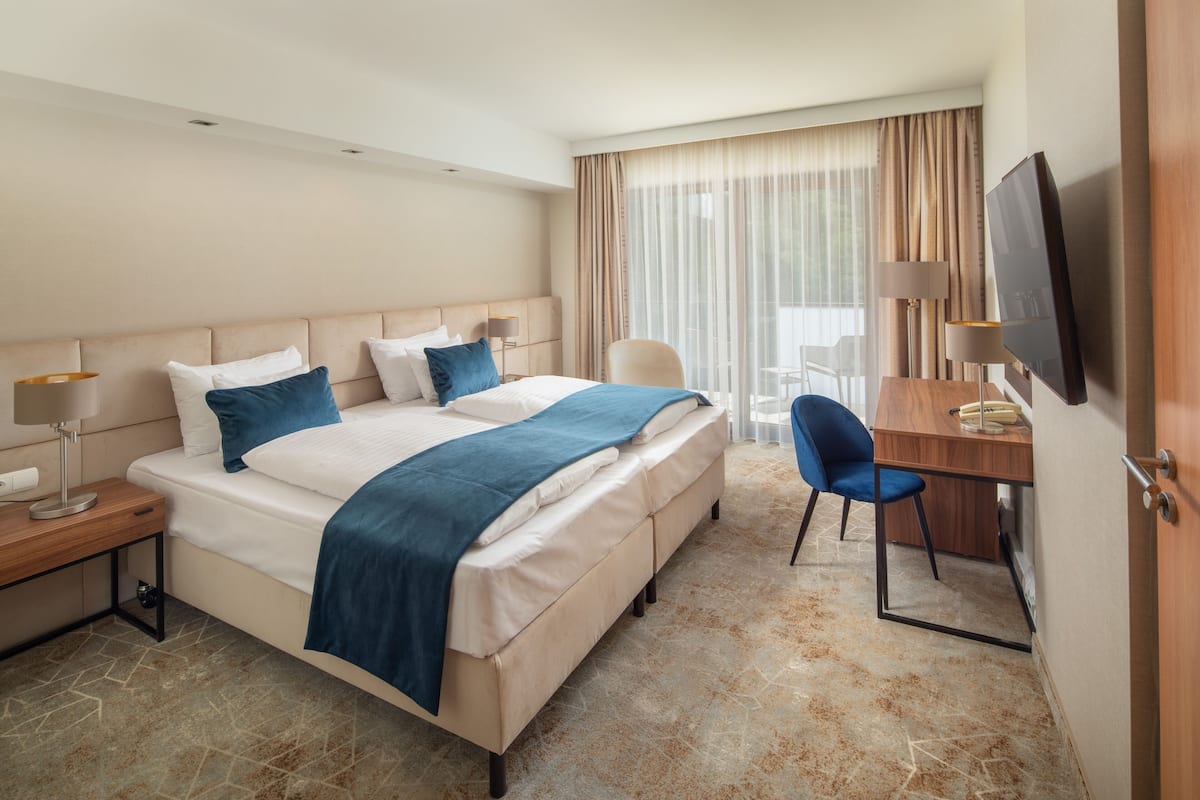 A hotel room with a bed, a desk, a chair, a TV, and a window with curtains.