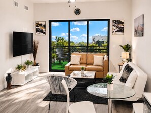 A modern living room with a sofa, coffee table, and chairs, a TV, and artwork on the walls.