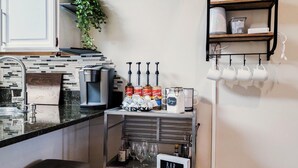 Et køkken med kaffemaskine, en bar med et skilt, og reoler med kopper og planter.