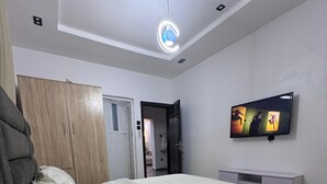 Un dormitorio con cama, armario, televisor y lámpara de techo.
