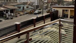 Balcón con baranda metálica que da a una calle con edificios y vehículos estacionados.