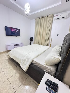A bedroom with a bed, a TV, an air conditioner, a bedside table, and a remote control.