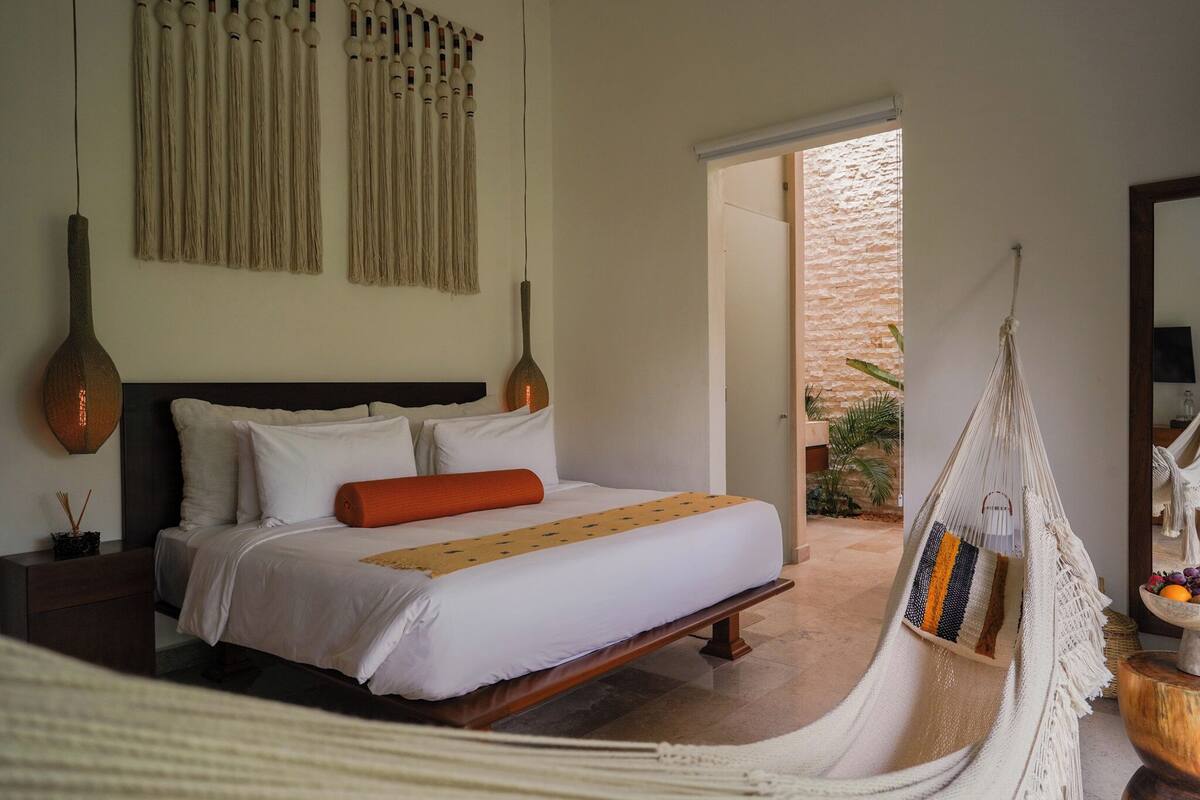 Une chambre à coucher avec un lit, des tables de chevet, un fauteuil suspendu et une vue sur l’extérieur.