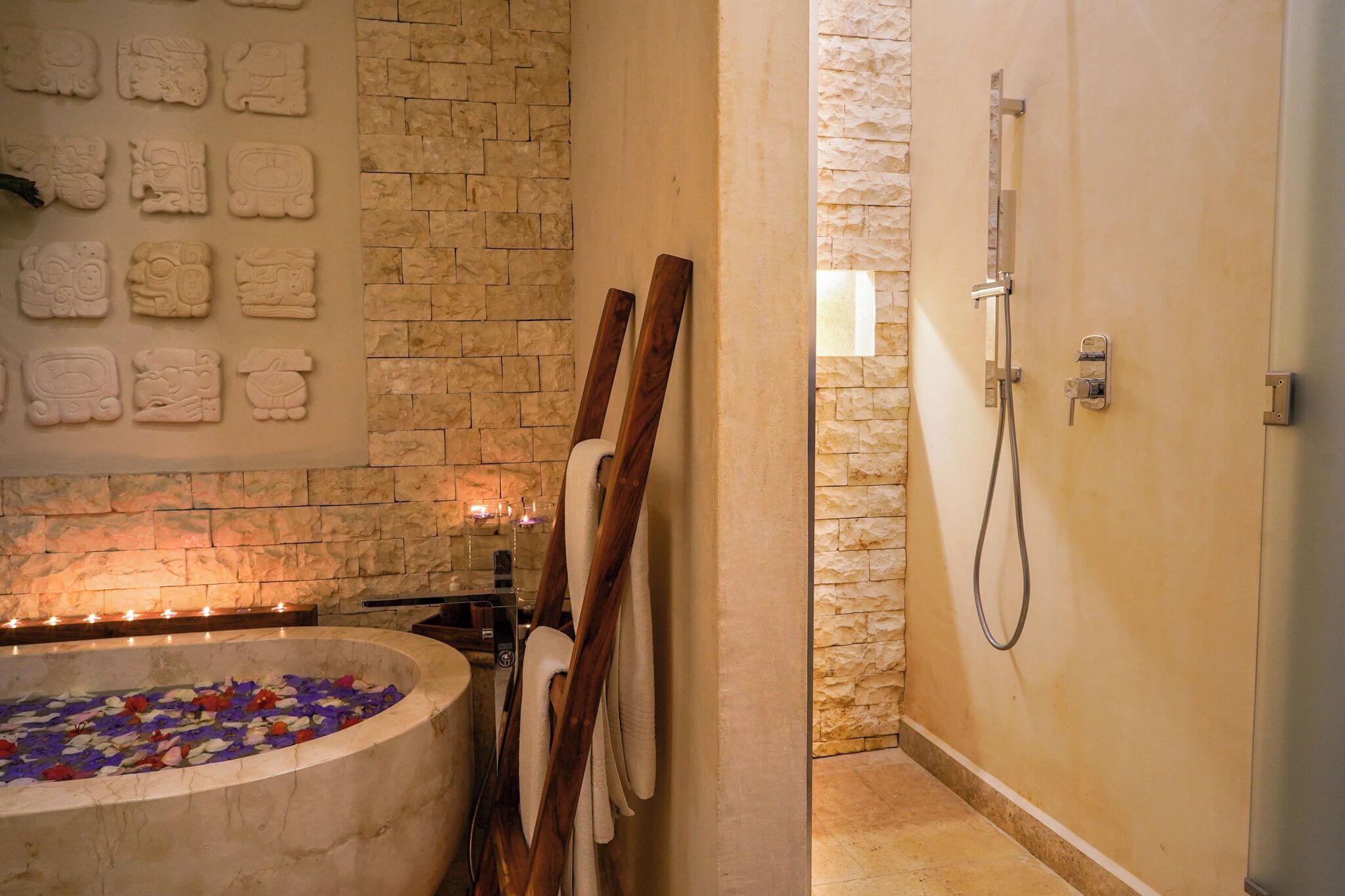 Un cuarto de spa con pared de piedra, una bañera llena de pétalos de rosa, bancos de madera y zona de ducha.