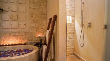 Un cuarto de spa con pared de piedra, una bañera llena de pétalos de rosa, bancos de madera y zona de ducha.