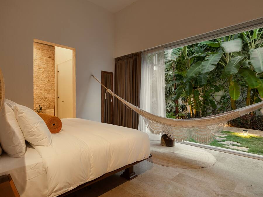 Un dormitorio con una cama grande, una hamaca y vistas a plantas tropicales a través de una ventana.