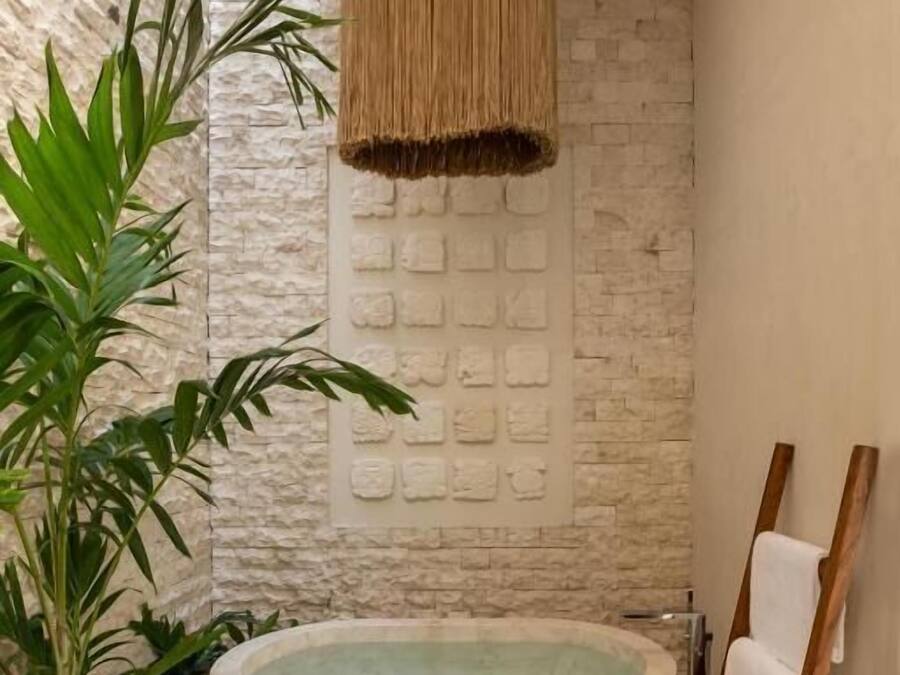 Un baño moderno con una bañera independiente, una pared de piedra texturizada y una lámpara colgante.