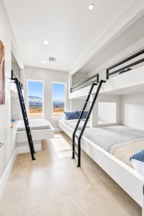 A modern bedroom with bunk beds, a window with a mountain view, and a ladder.