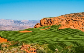 A golf course with sand bunkers and a mountainous backdrop.