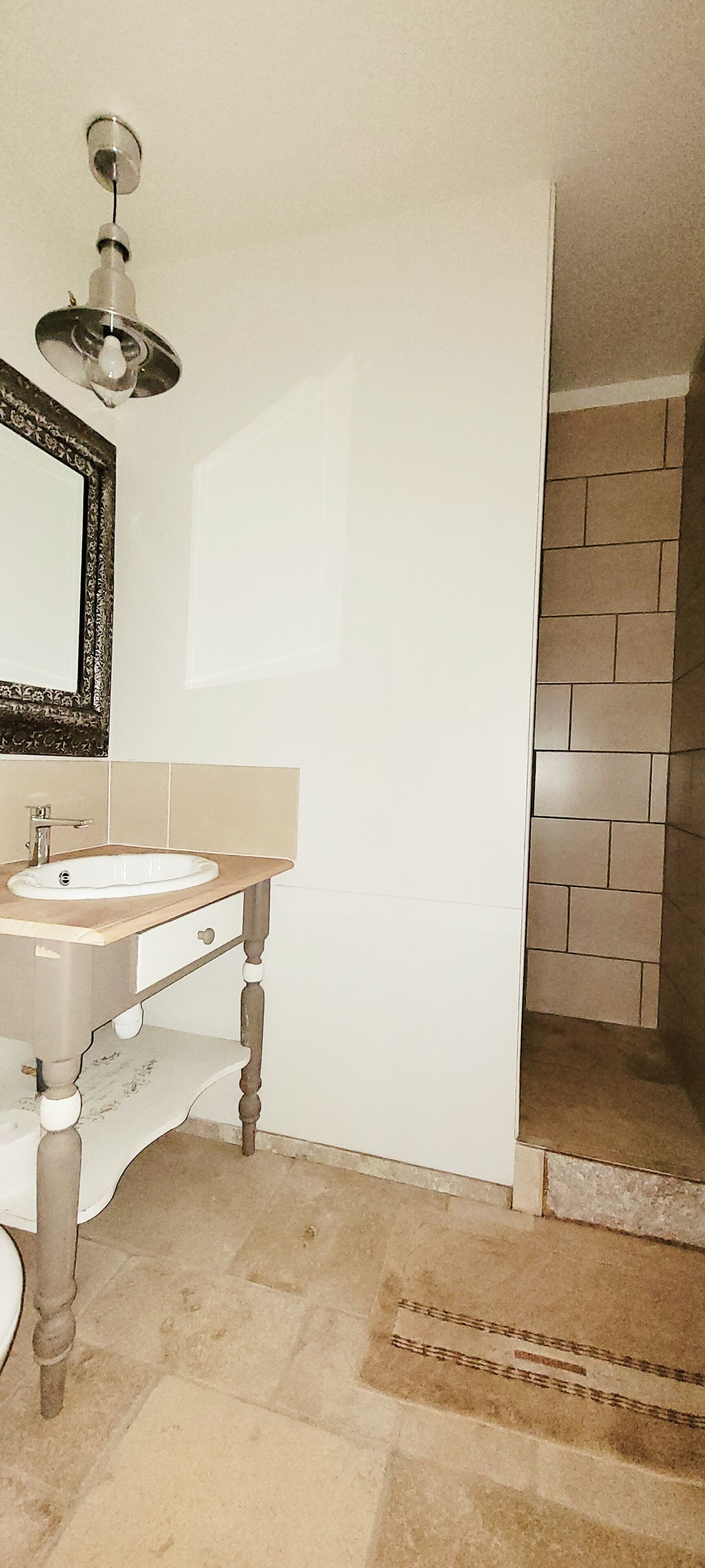 Un baño con un lavamanos blanco, un espejo con un marco ornamentado y una zona de ducha con paredes de azulejos.