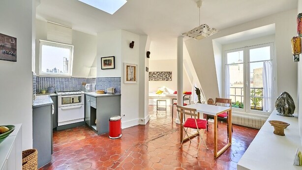 A modern kitchen with a skylight, a dining area with a table and chairs, and a view of the city through large windows.