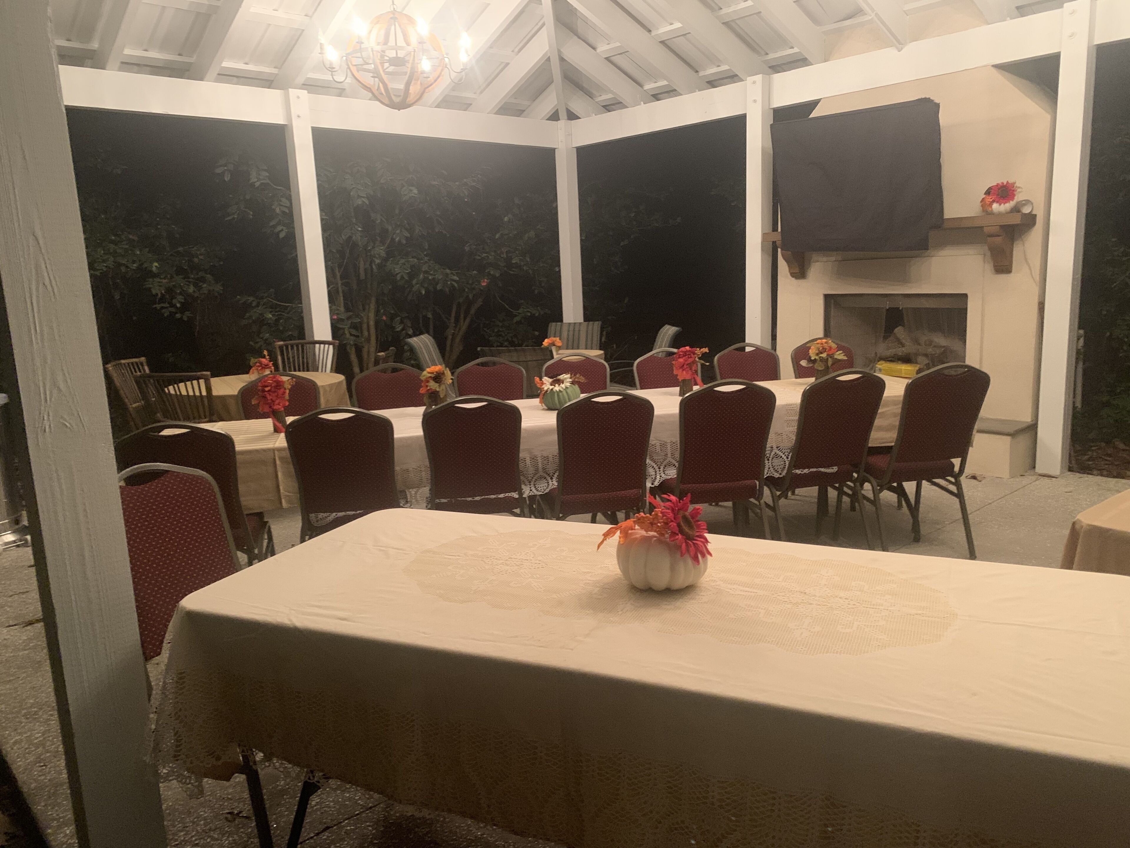 Un espacio exterior cubierto para comer, con mesas, sillas y una chimenea, y vistas al entorno.