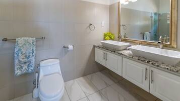 Un baño moderno con inodoro blanco, lavamanos con un espejo grande y toallero con toallas estampadas.