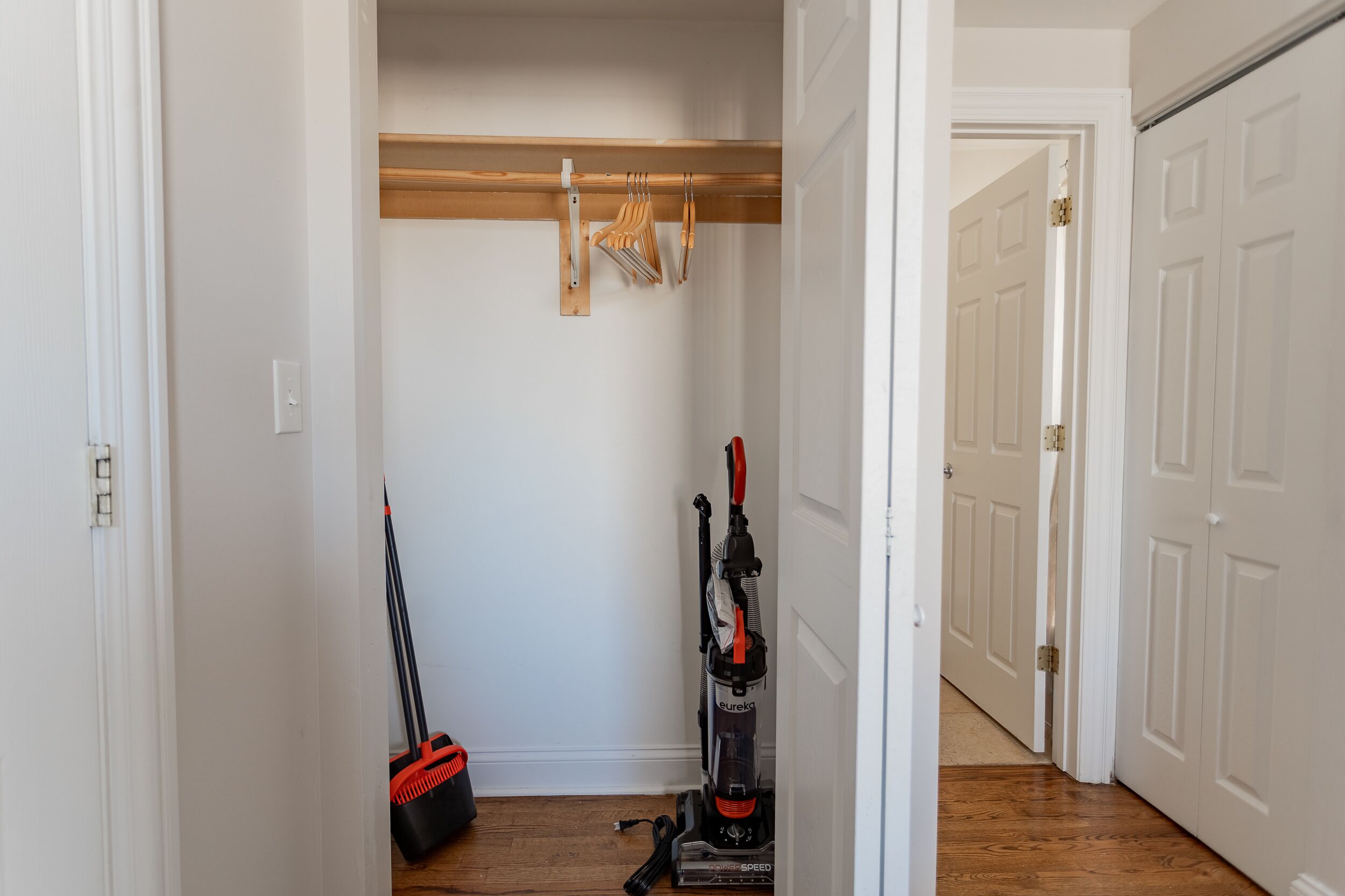 A hallway with a wooden floor, a vacuum cleaner, and a broom leaning against the wall.