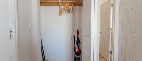 A hallway with a wooden floor, a vacuum cleaner, and a broom leaning against the wall.