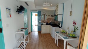 Eine kompakte Küche mit Essbereich, ausgestattet mit einem an der Wand montierten Fernseher, einem kleinen Tisch mit Stühlen und einem Blumentopf.