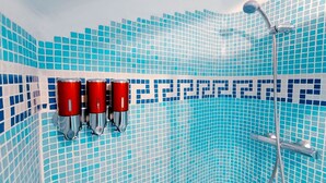Ein Badezimmer mit blauen Mosaikfliesen, drei roten Handtuchspendern und einer Duschbrause.