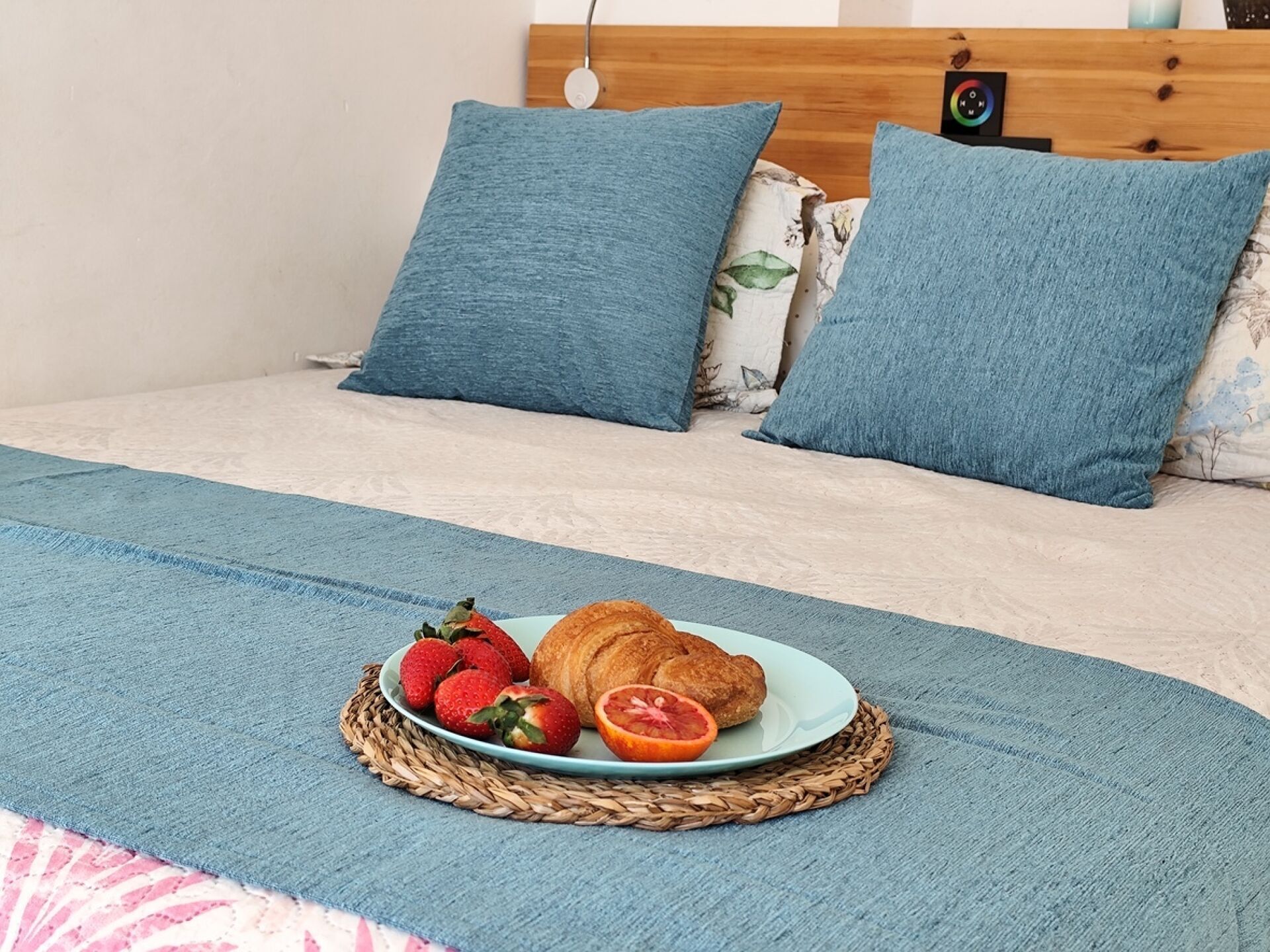 A bed with a blue blanket, a plate with strawberries and a croissant, and matching blue pillows.