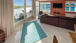 Een ruime woonkamer met een groot raam, een bank, een bijzettafeltje en een kamerbreed tapijt.