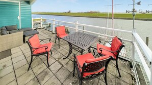 Een overdekt buitengebied met een tafel en stoelen, met uitzicht op een gracht en een molen op de achtergrond.