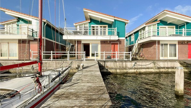 Een pand aan het water met een steiger, een zeilboot en een balkon.