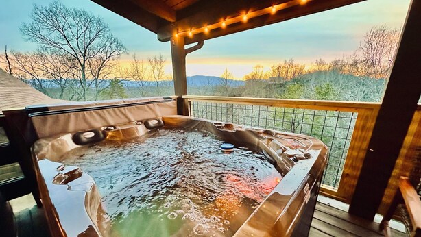 A hot tub on a wooden deck with a view of trees and hills.