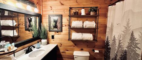 A wooden cabin bathroom with a sink, toilet, shelves with towels, and a mirror.