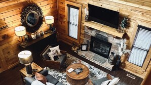 A cozy log cabin interior with a fireplace, a sofa, a coffee table, and a TV mounted on the wall.