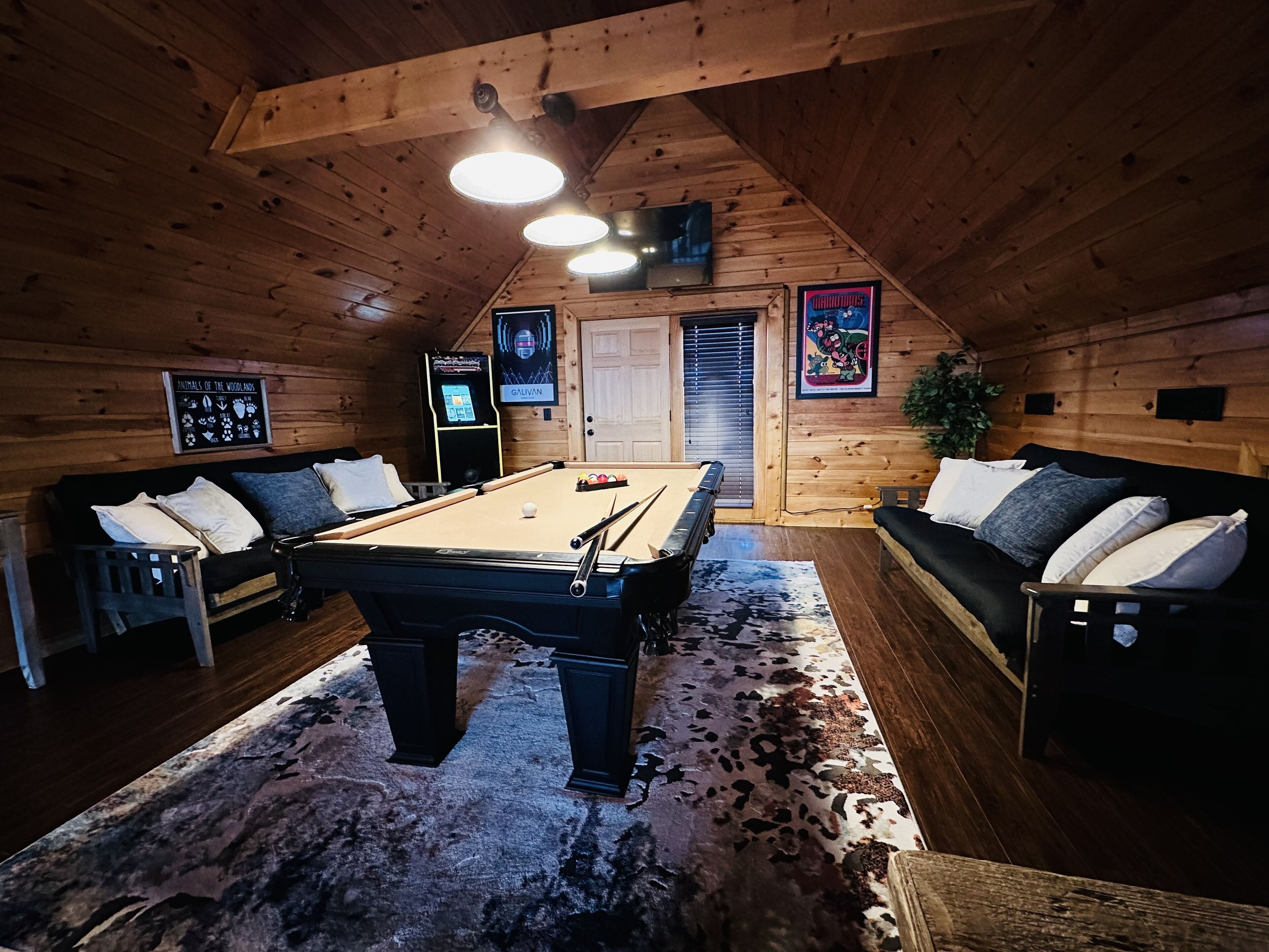 Une pièce confortable avec une table de billard, deux canapés, un ventilateur de plafond et une porte.