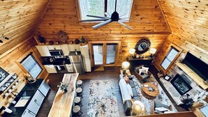 A spacious cabin with a kitchen, dining area, and living room, featuring wooden walls and a ceiling fan.