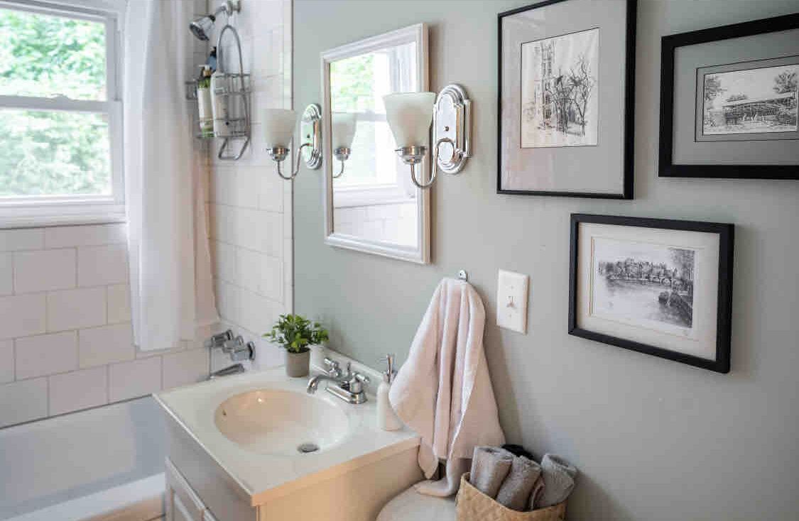 Ein Badezimmer mit Waschbecken, Spiegel, Handtuchhalter und gerahmten Bildern an der Wand.
