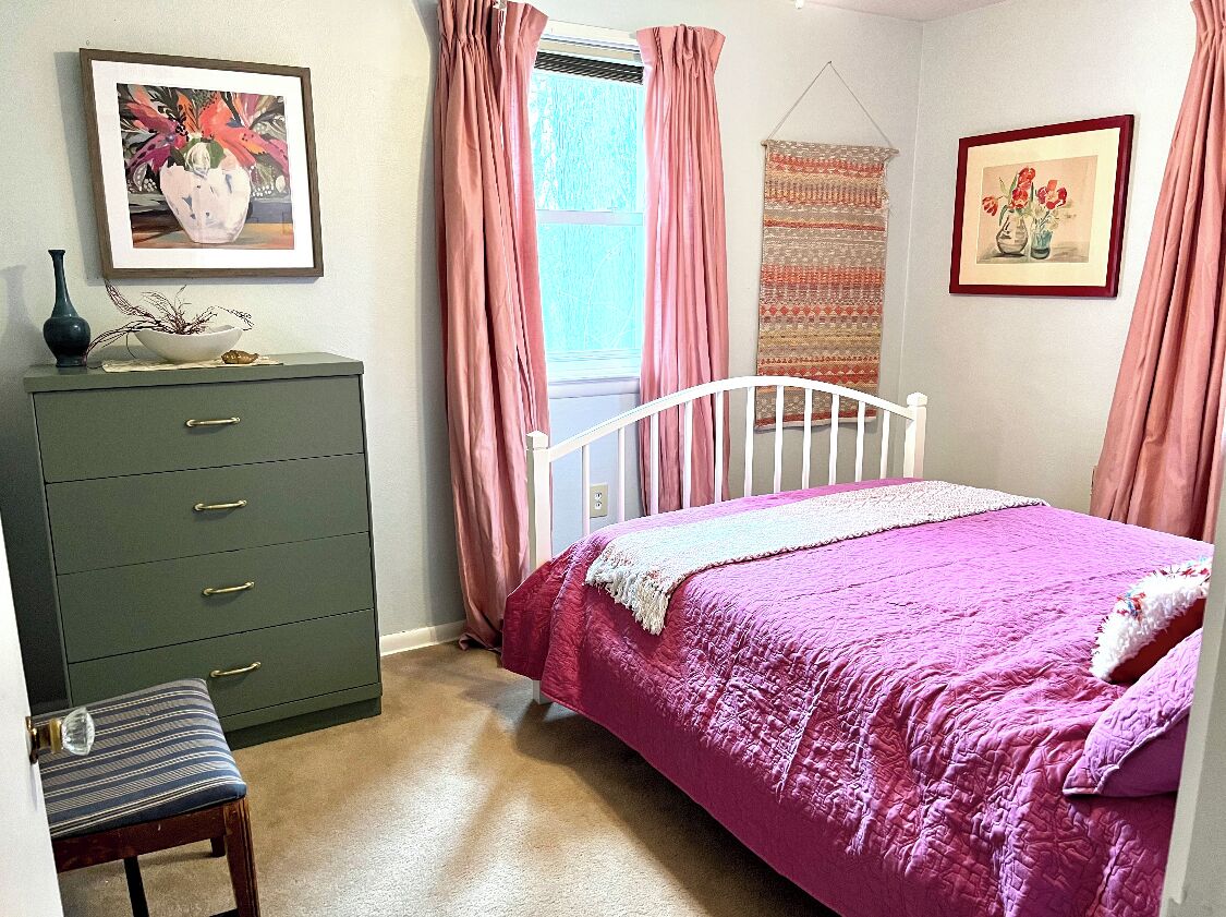 Une chambre à coucher avec un lit, une commode, une chaise et deux fenêtres ornées de rideaux roses.