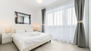 Ein modernes Schlafzimmer mit einem großen Bett, Nachttischen mit Lampen, einem Spiegel und durchsichtigen Vorhängen.